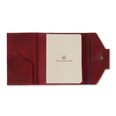 A red leather notebook organiser with a pen slider, closed with a regular book binding. The notebook appears to have a solid, smooth finish.